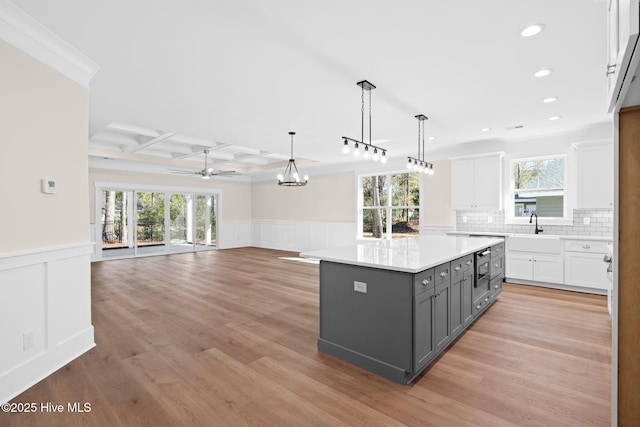 kitchen featuring gray cabinetry, decorative light fixtures, a kitchen island, a wealth of natural light, and white cabinets