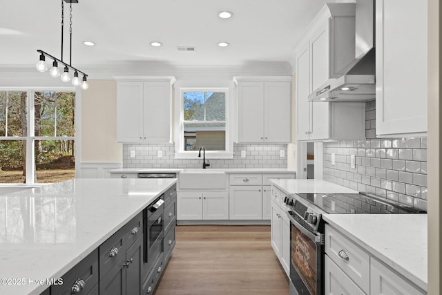 kitchen featuring range with electric cooktop, white cabinets, wall chimney range hood, pendant lighting, and sink