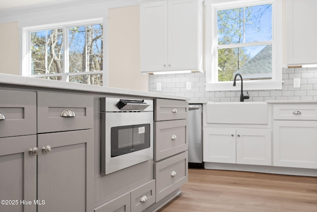 kitchen featuring light wood-type flooring, white cabinetry, backsplash, sink, and oven