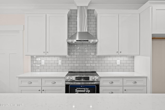 kitchen with wall chimney range hood, stainless steel range with electric stovetop, white cabinetry, and light stone countertops