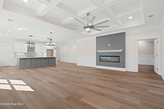 unfurnished living room with beam ceiling, light hardwood / wood-style floors, coffered ceiling, a fireplace, and ceiling fan with notable chandelier