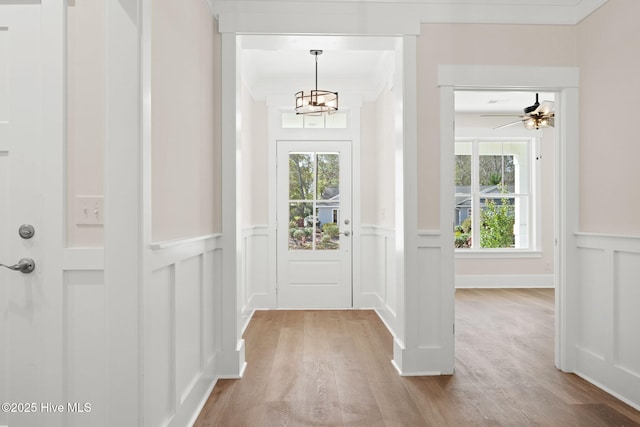 doorway with ornamental molding, light wood-type flooring, a chandelier, and a healthy amount of sunlight