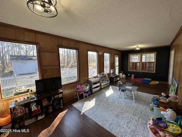 living room with wooden walls, ornamental molding, wood finished floors, and a healthy amount of sunlight