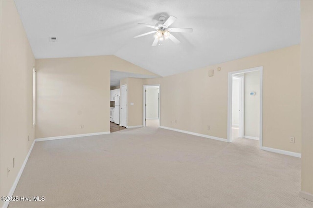 spare room featuring light colored carpet, visible vents, a ceiling fan, vaulted ceiling, and baseboards