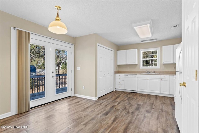 kitchen featuring white appliances, visible vents, white cabinets, pendant lighting, and a sink