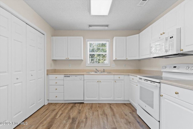 kitchen featuring light countertops, light wood-style flooring, white cabinets, a sink, and white appliances