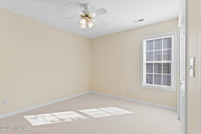 spare room featuring light colored carpet, visible vents, a ceiling fan, a textured ceiling, and baseboards