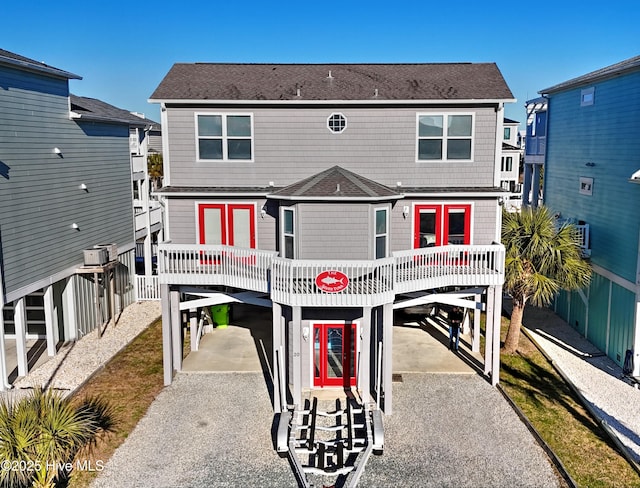 coastal home featuring a carport, roof with shingles, and gravel driveway