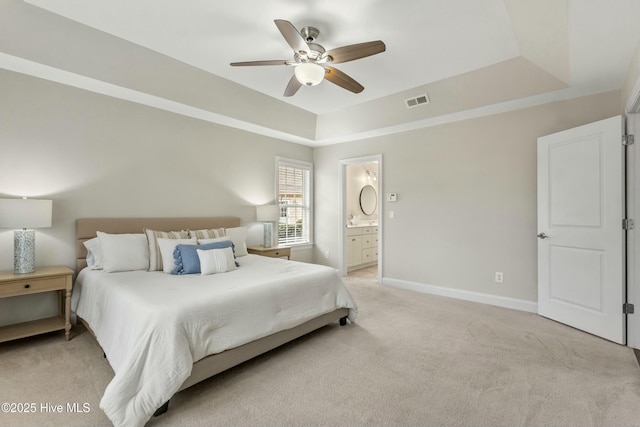 bedroom featuring ensuite bathroom, light colored carpet, visible vents, baseboards, and a raised ceiling