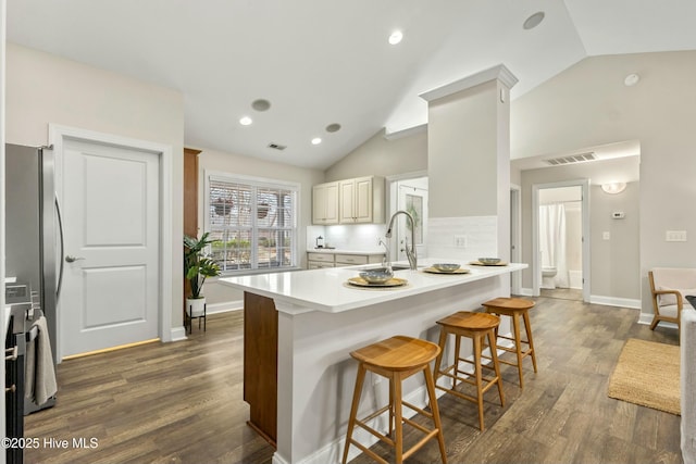 kitchen with dark wood-style floors, light countertops, visible vents, freestanding refrigerator, and a kitchen bar