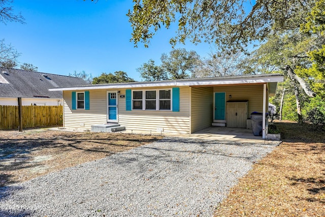 ranch-style house featuring a carport, gravel driveway, and fence