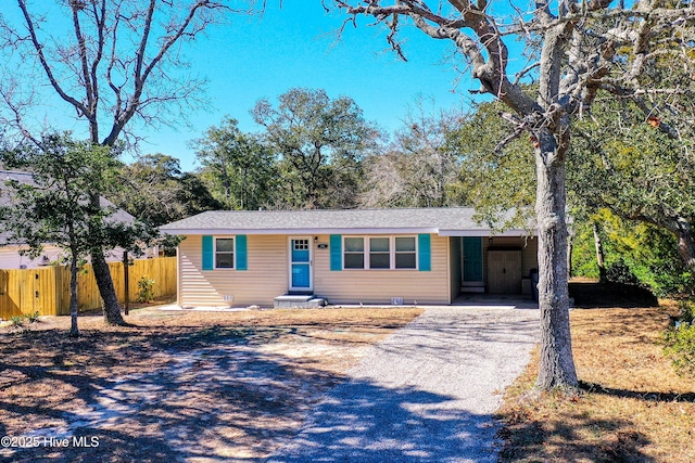 ranch-style home featuring an attached carport, gravel driveway, and fence