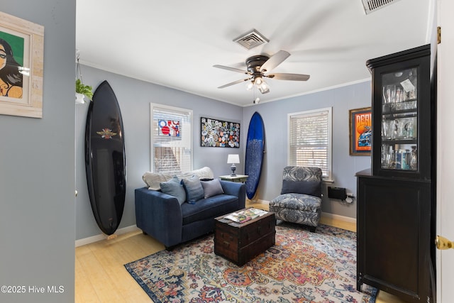 living room featuring visible vents, ornamental molding, a ceiling fan, wood finished floors, and baseboards