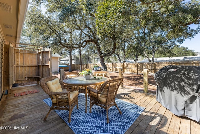 wooden terrace with outdoor dining area, area for grilling, and a fenced backyard