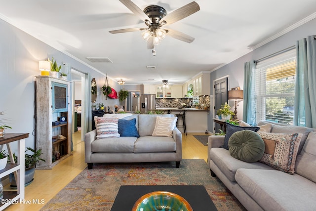 living area with light wood-type flooring, a ceiling fan, and crown molding