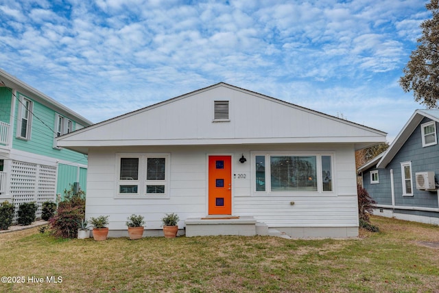 bungalow-style house with an AC wall unit and a front lawn