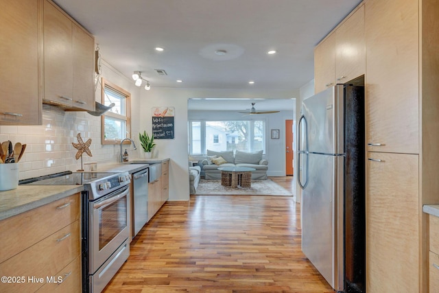 kitchen with light wood finished floors, stainless steel appliances, light countertops, decorative backsplash, and open floor plan