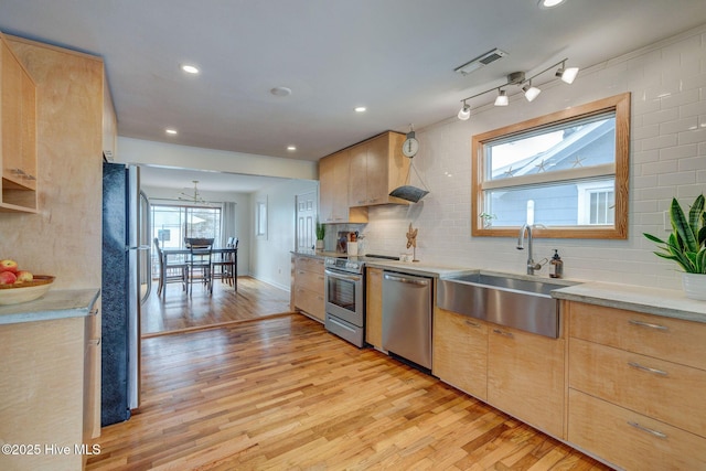 kitchen with a sink, light wood-style floors, light countertops, appliances with stainless steel finishes, and light brown cabinetry