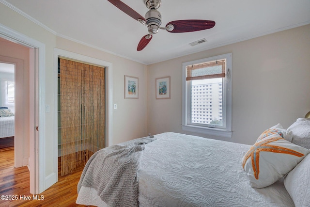 bedroom featuring ornamental molding, visible vents, light wood finished floors, and a ceiling fan