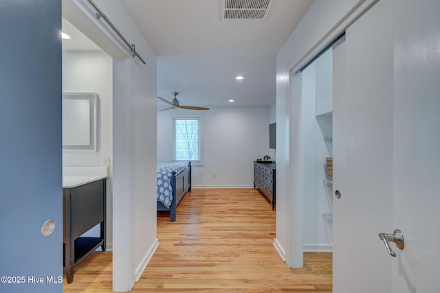 corridor featuring light wood finished floors, recessed lighting, visible vents, a barn door, and baseboards