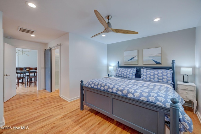 bedroom with light wood finished floors, a barn door, visible vents, baseboards, and recessed lighting