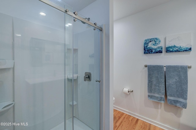 bathroom with baseboards, a shower stall, toilet, and wood finished floors