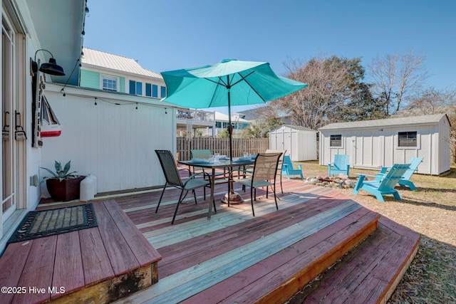 wooden deck with a storage unit, an outdoor structure, outdoor dining space, and fence