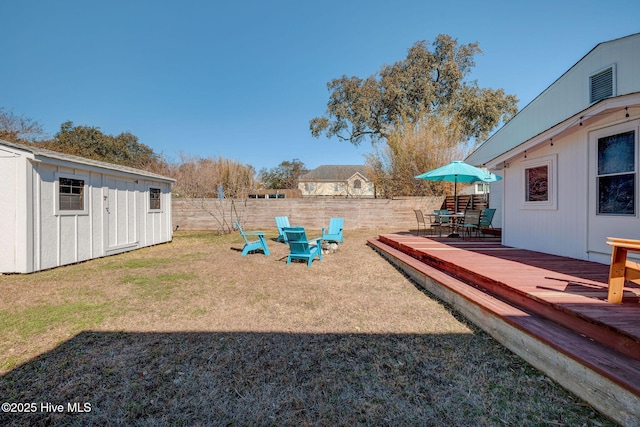 view of yard featuring a storage shed, a fenced backyard, a deck, an outdoor structure, and outdoor dining space