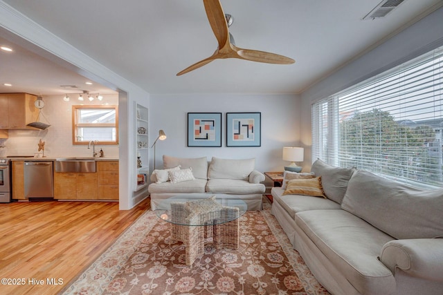 living room featuring light wood-style flooring, visible vents, a ceiling fan, and ornamental molding