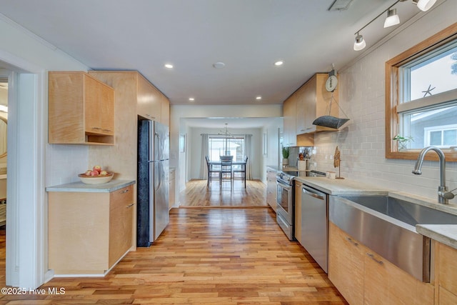 kitchen with light wood-style flooring, stainless steel appliances, a sink, light countertops, and tasteful backsplash