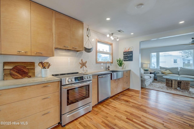 kitchen featuring light brown cabinets, stainless steel appliances, a sink, and open floor plan