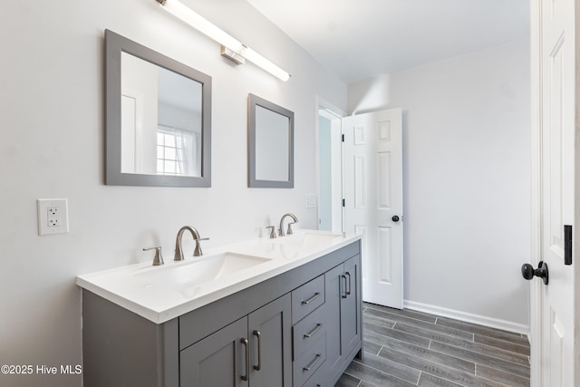 full bathroom featuring wood finish floors, a sink, baseboards, and double vanity