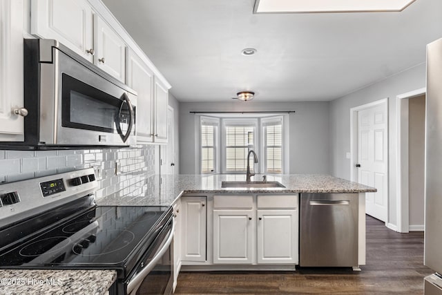 kitchen featuring appliances with stainless steel finishes, white cabinets, a sink, and a peninsula