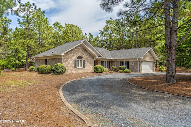 ranch-style house with curved driveway, brick siding, an attached garage, and a shingled roof