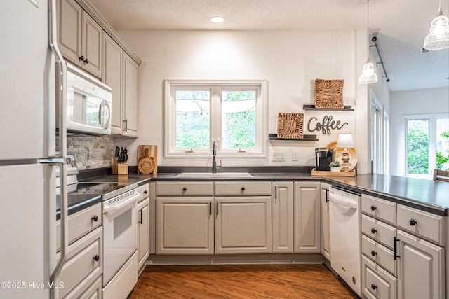 kitchen with white appliances, dark countertops, a sink, a peninsula, and dark wood finished floors