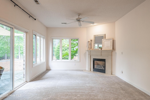 unfurnished living room with carpet, a fireplace with flush hearth, a textured ceiling, a ceiling fan, and baseboards