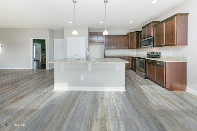 kitchen featuring light wood-style flooring, appliances with stainless steel finishes, a sink, an island with sink, and baseboards