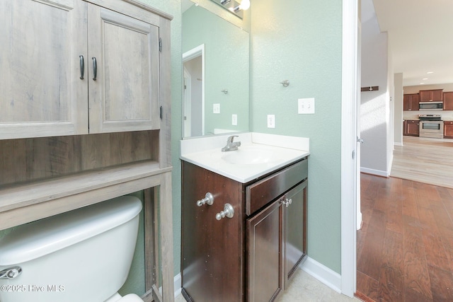 half bath with toilet, vanity, baseboards, and wood finished floors