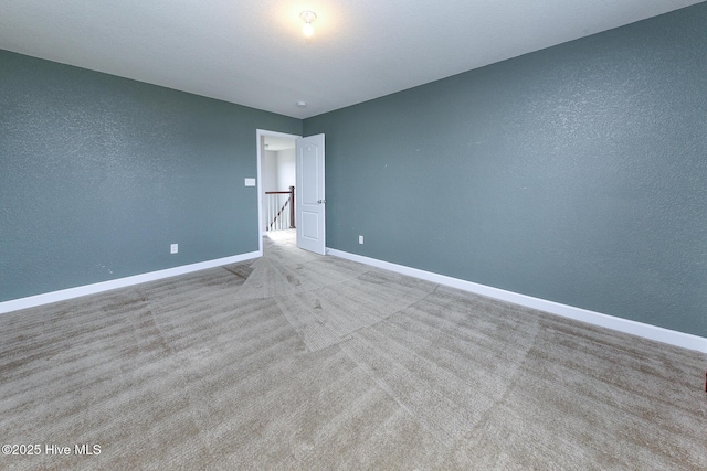 unfurnished room with carpet floors, a textured wall, and baseboards