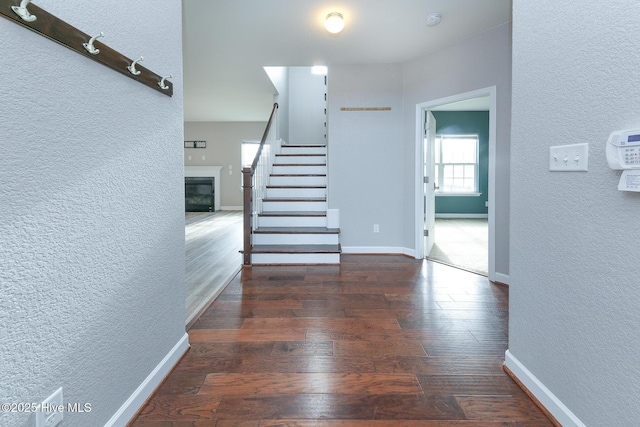 interior space featuring a glass covered fireplace, a textured wall, baseboards, and wood finished floors