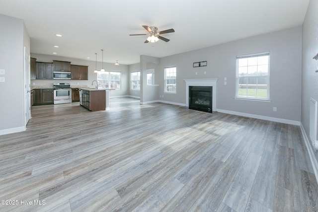 unfurnished living room featuring light wood-type flooring, recessed lighting, baseboards, and a glass covered fireplace