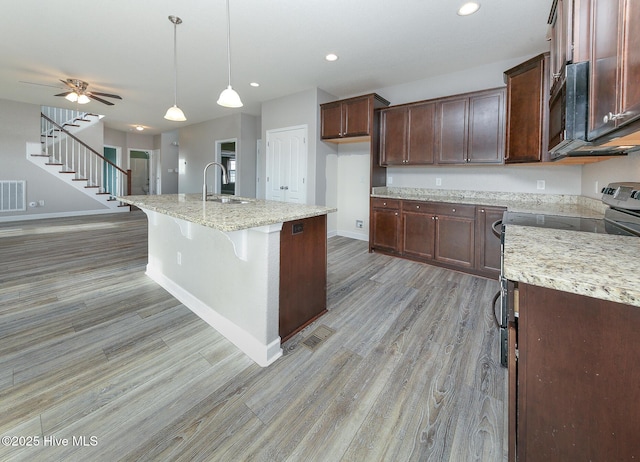 kitchen with light wood-type flooring, light stone countertops, black microwave, and a sink