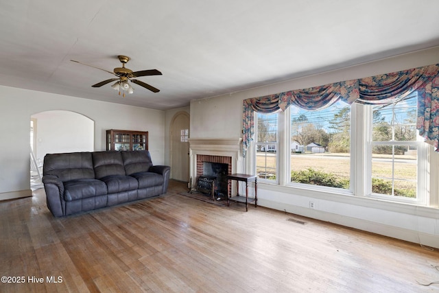 living area with wood-type flooring, a fireplace, visible vents, and a ceiling fan
