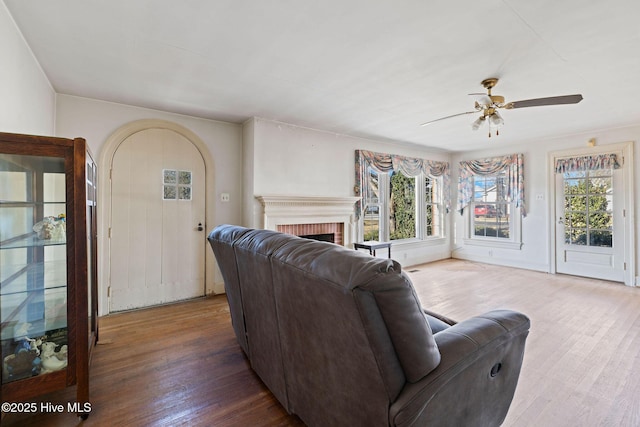 living area with dark wood-type flooring, a brick fireplace, and a ceiling fan