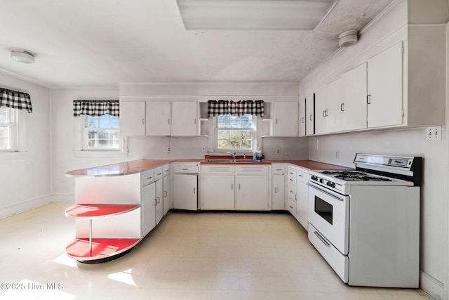 kitchen with baseboards, light countertops, white gas stove, white cabinetry, and a sink
