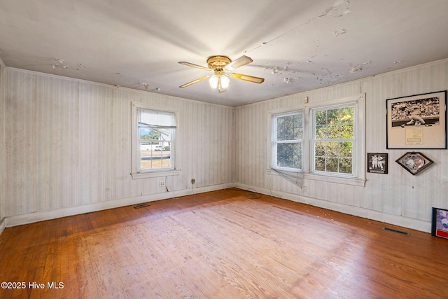 empty room featuring a healthy amount of sunlight, visible vents, and wood finished floors