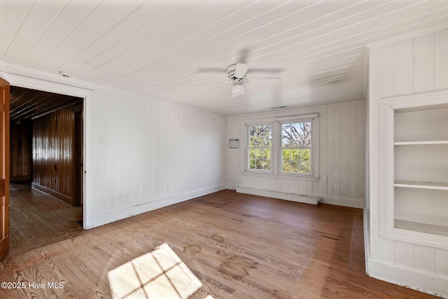empty room featuring a baseboard radiator, ceiling fan, baseboards, and wood finished floors