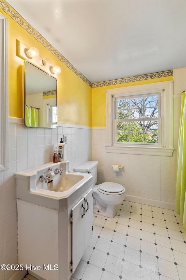 bathroom with toilet, wainscoting, vanity, and tile walls