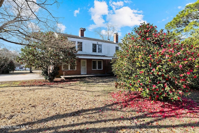 rear view of property with a porch, brick siding, a yard, and a chimney