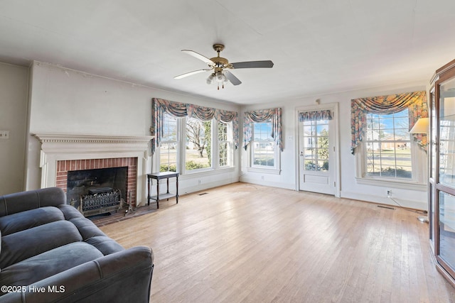 living room featuring light wood-style floors, a fireplace, ceiling fan, and baseboards